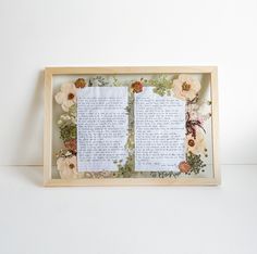 an open book with paper flowers and leaves on it is displayed in a wooden frame