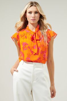 This top is like waking up to the brightest sunrise. Bold fuchsia floral motifs lay against this bright orange-ground. The vibrant print takes on the Cassius Blouse, featuring a tie neck detail to create a cut out at the chest. Pintuck pleats add a sweet touch to the shoulder, framing flutter cap sleeves. Wear it tucked in high waisted trousers for a completed look.- Tie neck detail- Lined- Pintuck pleats- Relaxed fit- Color: Fuchsia OrangeSize + Fit - Model is 5'10" and wearing size XS- Measure Spring Bold Print Orange Tops, Summer Printed Tie Neck Tops, Printed Tie Neck Tops For Summer, Summer Floral Print Tie Neck Top, Summer Orange Tops With Bold Print, Orange Bold Print Summer Top, Orange Tops With Bold Print For Summer, Vibrant Yellow Floral Print Tops, Orange Blouse With Vibrant Print For Spring