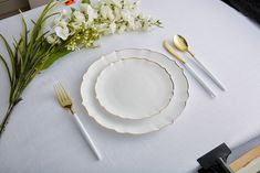 a table set with white and gold plates, silverware, and flowers on it