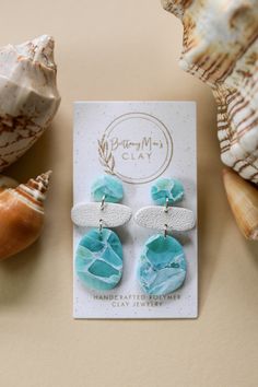 two sea glass earrings on top of a card next to seashells and shells