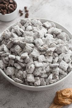 a white bowl filled with dog food next to a wooden spoon and some chocolate chips