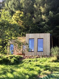 a small wooden cabin sitting in the middle of a lush green field next to trees