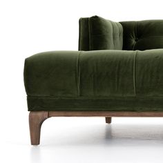 a green couch sitting on top of a white floor next to a wooden leg chair