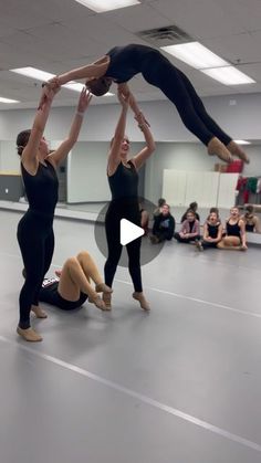 three women are doing acrobatic tricks in an indoor gym while others watch