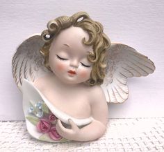 an angel figurine holding a white vase with pink roses on it's side