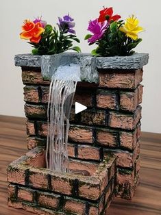 a water fountain with flowers in it on top of a wooden table next to a brick wall