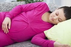 a pregnant woman laying on top of a couch with her arms behind her back and eyes closed