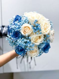 a bouquet of blue and white flowers in someone's hand with a camera behind it