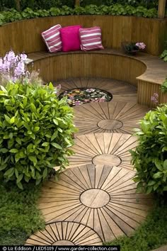 a circular bench in the middle of some bushes and trees with pink pillows on it