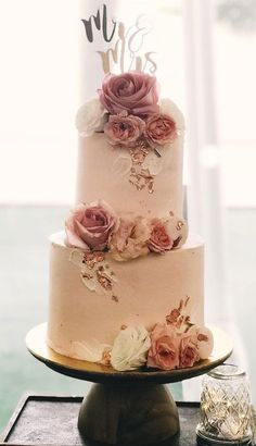 a wedding cake with pink flowers and mr and mrs topper on the bottom tier