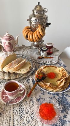 a table topped with plates and bowls filled with food next to a tea pot on top of a lace covered table cloth