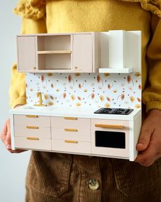 a person holding a doll house kitchen set in their hands, with the cabinets open