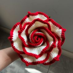 a crocheted red and white rose is held in someone's hand,