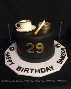 a black and white birthday cake with gold numbers on it's side, topped with a coffee mug