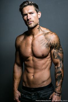 a shirtless man with tattoos on his chest posing for a black and white photo