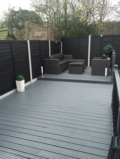 an outdoor deck with wicker furniture and potted plants on the side, in front of a black fence