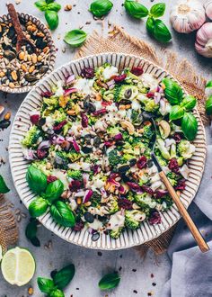 a person holding a spoon in a bowl filled with salad next to garlic and lemons