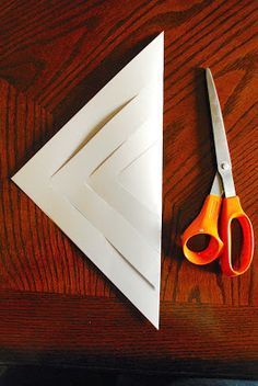 scissors and paper cut out to look like an arrow on a wooden table next to a pair of scissors