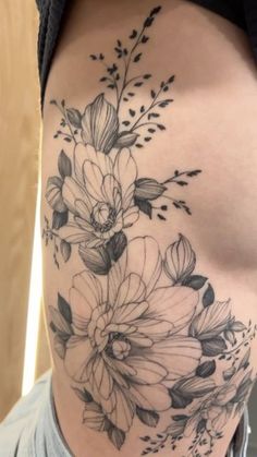 a woman's stomach with flowers and leaves tattooed on the side of her body