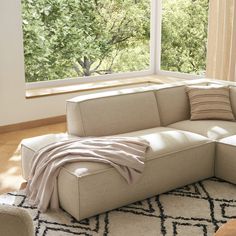 a living room with a large sectional couch in front of a window and a rug on the floor