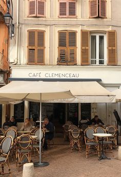 people sitting at tables under an umbrella in front of a building