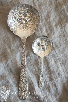 two silver spoons sitting next to each other on top of a cloth covered table