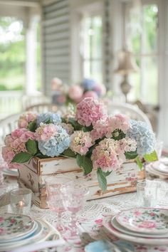 the table is set with pink and blue flowers in a wooden box on top of it