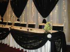 a long table with black and white drapes draped over it, decorated with flowers