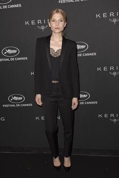 a woman standing in front of a black wall wearing a suit and heels with her hands on her hips