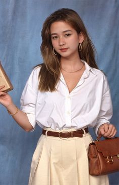 a young woman is holding a purse and posing for a photo in front of a blue background