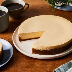 a cheesecake sitting on top of a white plate next to two cups of coffee