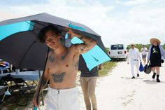 a shirtless man holding an umbrella while walking down the road with other people behind him