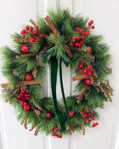 a christmas wreath hanging on the front door with holly and red berries, pine cones and cinnamon sticks