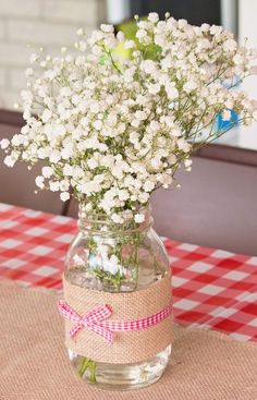 a vase filled with white flowers sitting on top of a red and white checkered table cloth