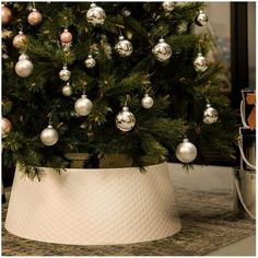 a christmas tree in a white pot with ornaments hanging from it's top and bottom