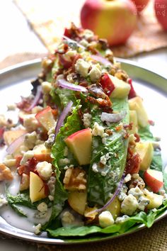 a salad with lettuce, apples, cheese and nuts in it on a plate