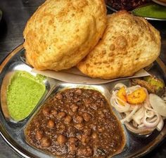 some food is on a metal plate with sauces and other foods around it, including bread