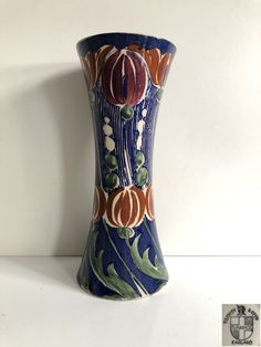 a blue vase with orange and green designs on the bottom is sitting on a white surface