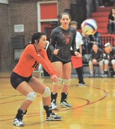 two women playing volleyball on a court with people watching from the sidelines behind them