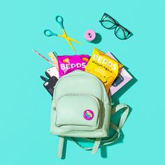 the contents of a backpack laid out on a blue surface with scissors, eyeglasses and other items