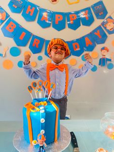 a young boy standing in front of a blue and orange birthday cake with decorations on it