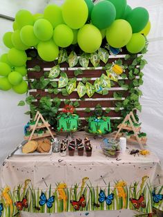 a table topped with lots of green balloons next to a wooden crate filled with cake