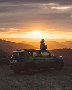 a person standing on top of a green car in the mountains at sunset or sunrise