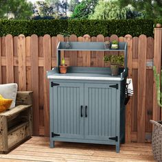 an outdoor potting bench and cabinet on a deck in front of a wooden fence