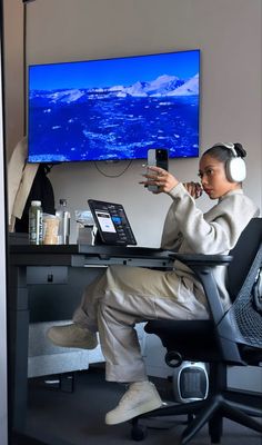 a woman sitting at a desk with headphones on and looking at her cell phone