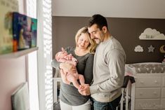 a man and woman are holding a baby in their arms while standing next to a crib