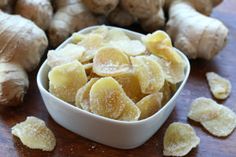 a white bowl filled with sliced up bananas next to some ginger chips on a wooden table