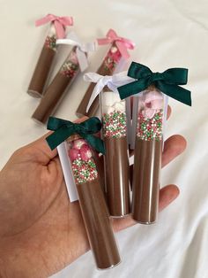 hand holding four brown and white candy tubes with flowers on them, tied with green ribbon