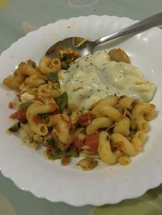 a white plate topped with pasta covered in sauce and cheese next to a spoon on a table