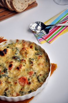 a casserole dish on a table with bread and utensils